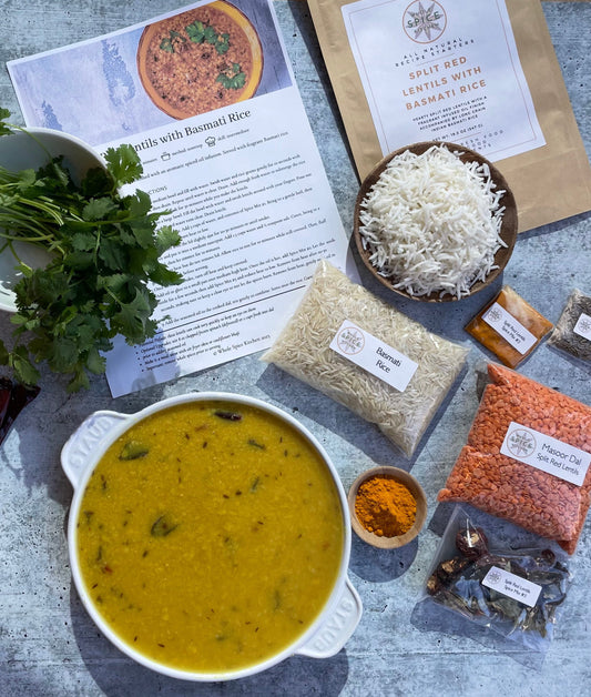 Pot of cooked yellow lentils,  Basmati Rice, bright orange split red lentils, orange turmeric, dark green cilantro, recipe, and brown kraft package, all on a gray countertop