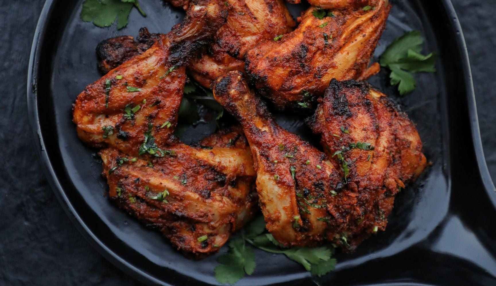 Charred grilled Tandoori Chicken with Cilantro on a black pate